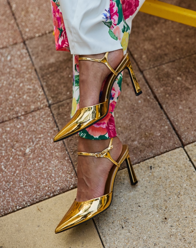 Gold pointed-toe heels with floral print trousers on stone tile